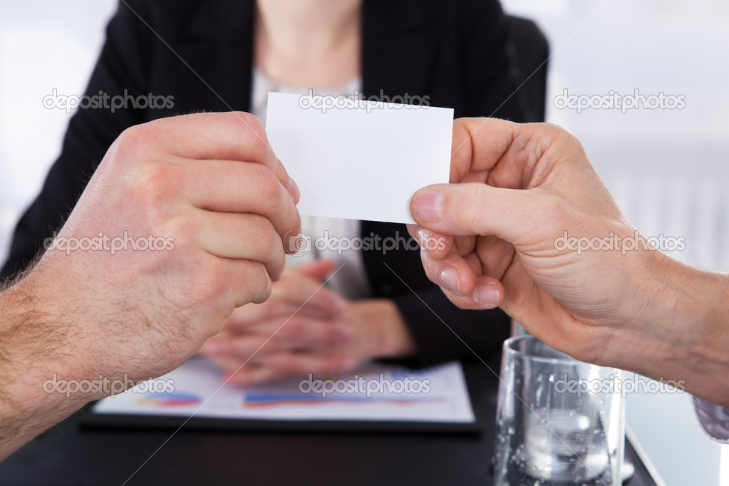 Exchanging Visiting Card In Front Of Colleague At Office Desk