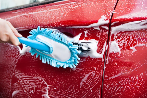 Main avec brosse bleue lavage voiture rouge — Photo
