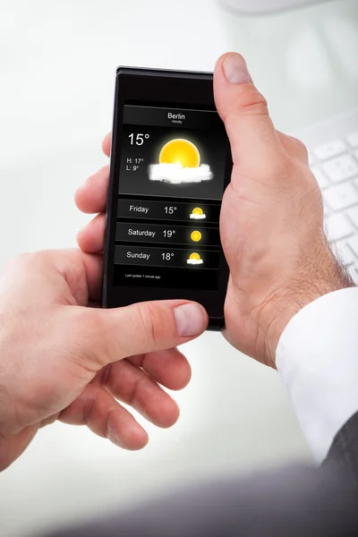 Бизнесмен смотрит прогноз погоды на сотовый телефон — стоковое фото
