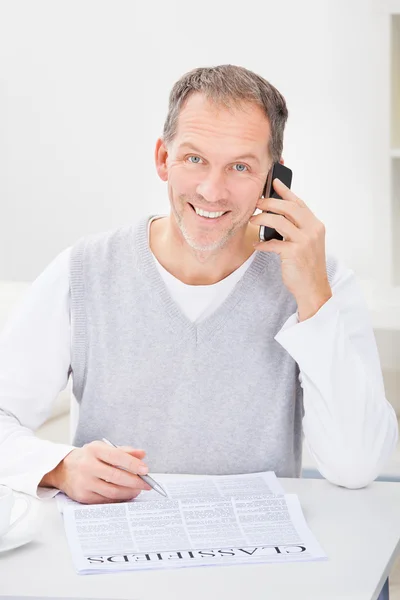 Mannen framför tidningen talar i mobiltelefon — Stockfoto