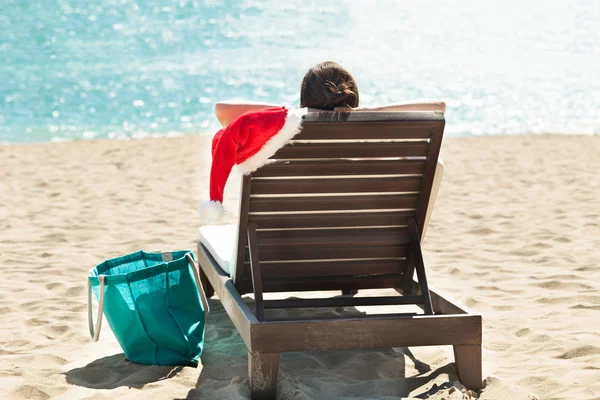 Woman with Santa hat relaxing on deck chair at beach resort — Stock Photo, Image