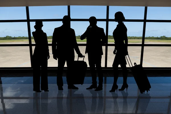 Businesspeople with luggage standing against airport window — Stock Photo, Image