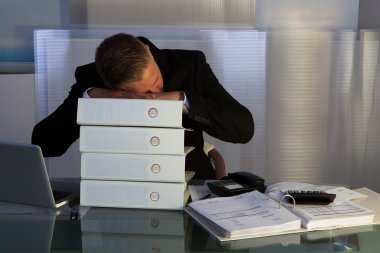 Exhausted businessman sleeping an a stack of files clipart