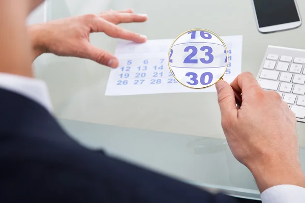 Бизнесмен смотрит на календарь через увеличительное стекло — стоковое фото