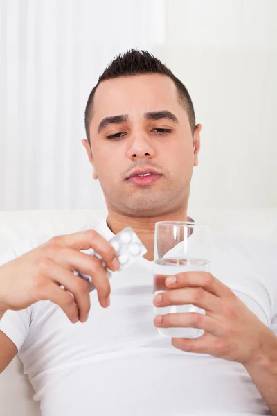Hombre con paquete de píldoras y vaso de agua — Foto de Stock