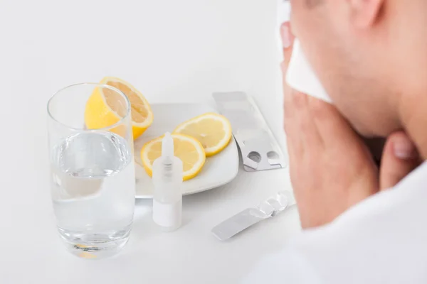 Homem que sofre de frio com medicamentos e vidro de água na mesa — Fotografia de Stock