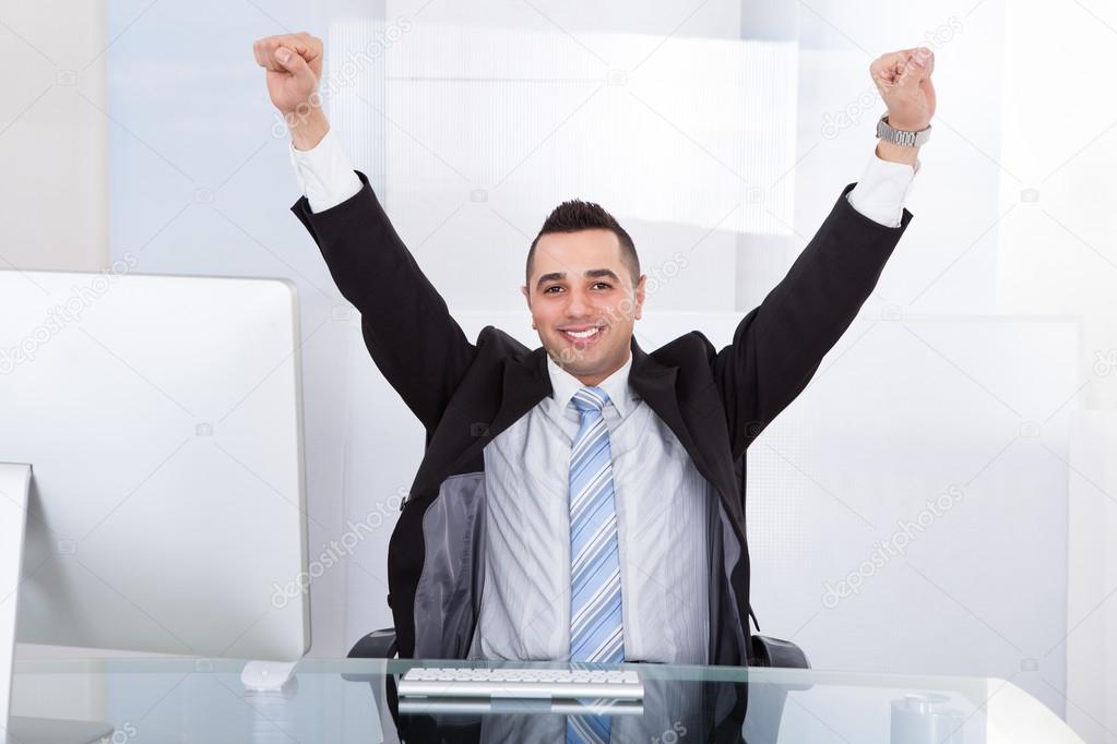 Businessman With Arms Raised Sitting At Computer Desk