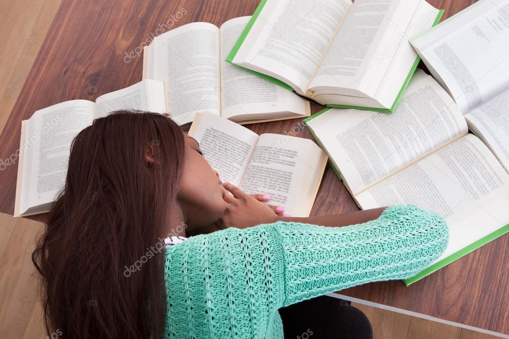 Female student sleeping with books at classroom desk
