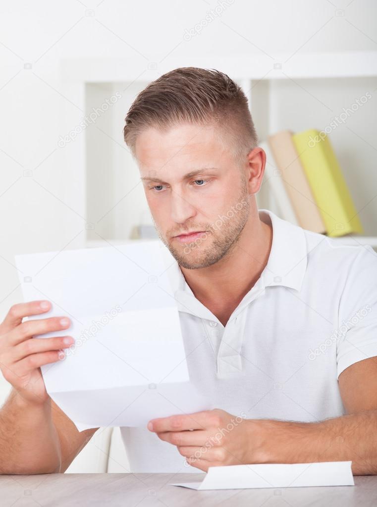 Man sitting reading a letter with a serious expression