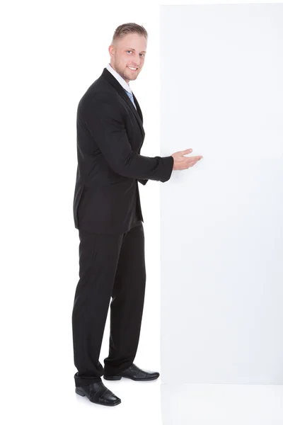 Stylish businessman pointing to a blank white sign — Stock Photo, Image