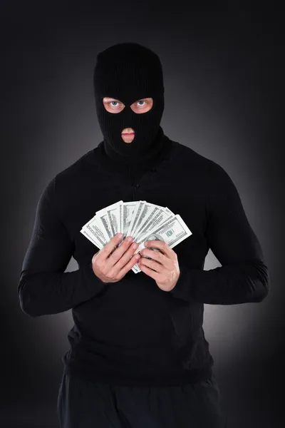 Criminal in a balaclava holding a fistful of money — Stock Photo, Image