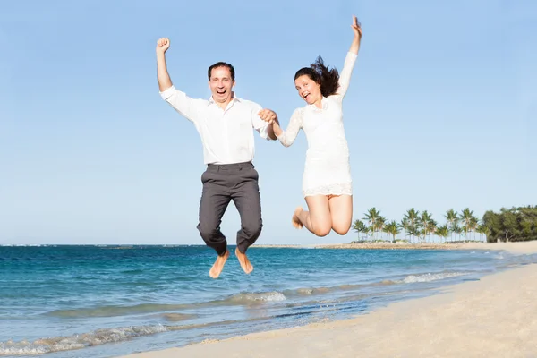 Aufgeregtes Paar hält Händchen beim Sprung am Strand — Stockfoto