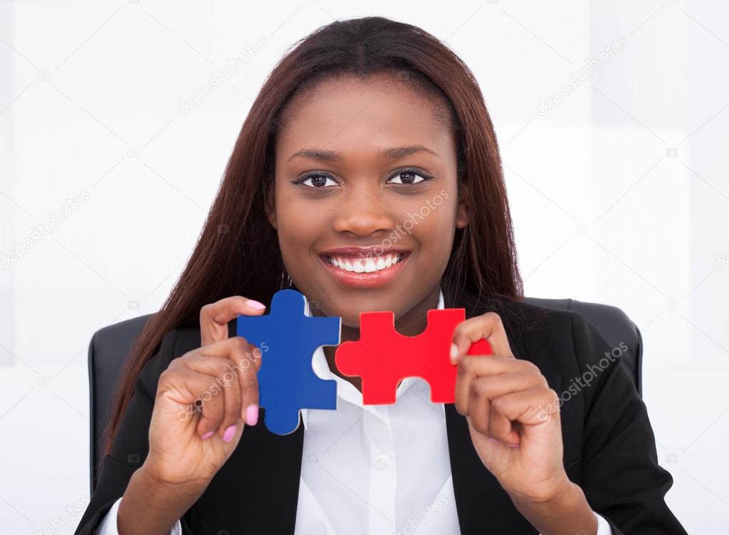 Confident businesswoman holding puzzle pieces in office