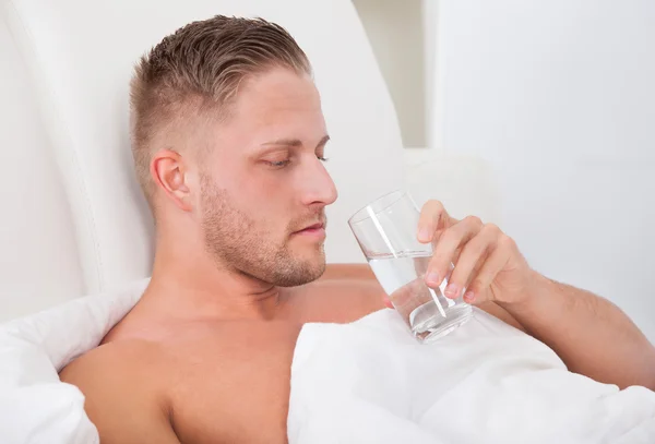 Uomo che beve un bicchiere d'acqua a letto — Foto Stock