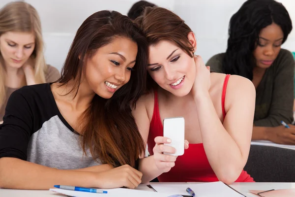 Gelukkig vrouwelijke studenten met behulp van mobiele telefoon in klas — Stockfoto