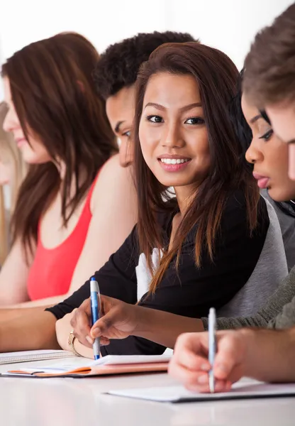 Kobiet student siedział z kolegami, pisanie na biurko — Zdjęcie stockowe