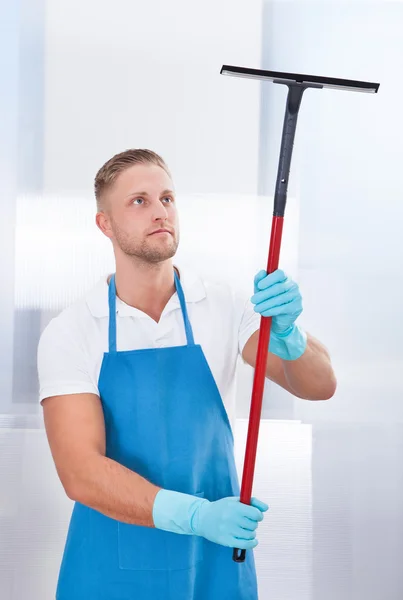 Male janitor using a squeegee to clean a window — Stock Photo, Image