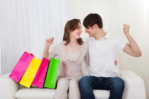 Casal feliz sentado no sofá com sacos de compras — Fotografia de Stock