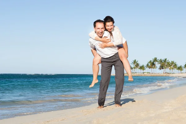 Man geven piggyback rit naar vrouw aan het strand — Stockfoto