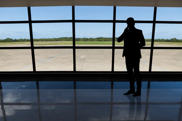 Podnikatel využívá mobilní telefon proti letišti okno — Stock fotografie