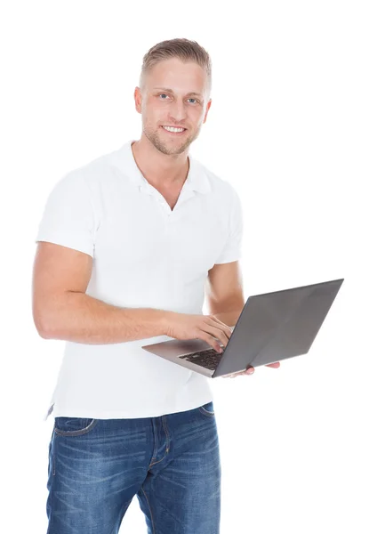 Smiling man in jeans standing using a handheld laptop computer — Stock Photo, Image