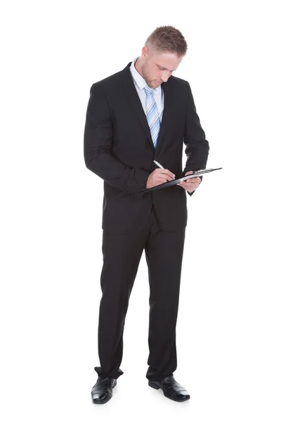 Geschäftsmann steht schreibend auf einem Klemmbrett — Stockfoto