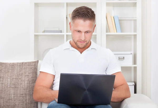 Junger Mann sitzt in seinem Wohnzimmer auf dem Sofa und benutzt einen Laptop — Stockfoto