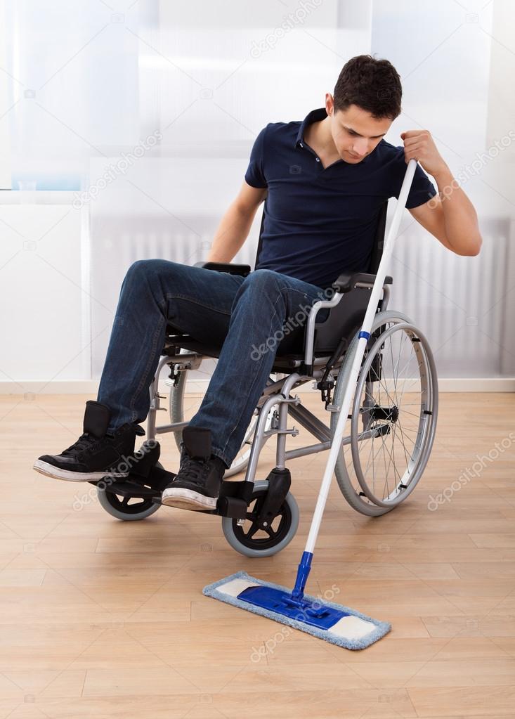 Handicapped Man Mopping Floor While Sitting On Wheelchair