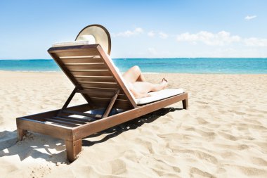 Woman Sunbathing On Deck Chair At Beach clipart
