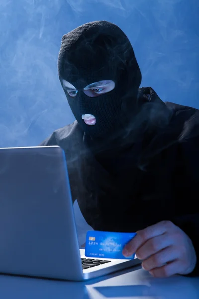 Hacker drží kreditní karty při používání notebooku — Stock fotografie