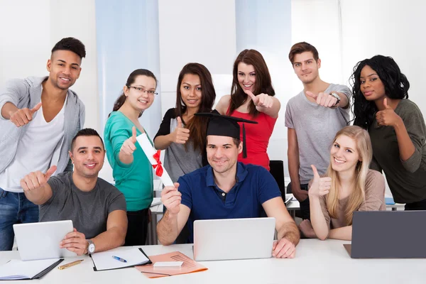 Étudiant tenant le degré avec des camarades de classe gesticulant pouces vers le haut — Photo