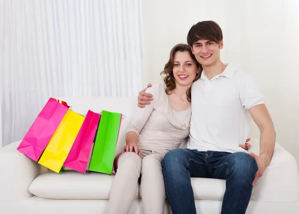 Casal feliz sentado no sofá com sacos de compras — Fotografia de Stock