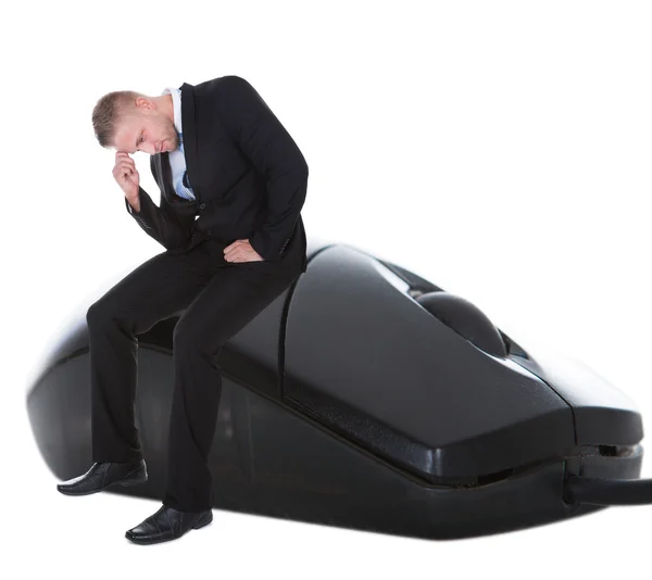 Worried businessman sitting on a computer mouse — Stock Photo, Image