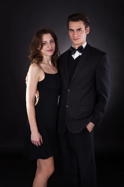 Elegante pareja de pie sobre fondo negro — Foto de Stock