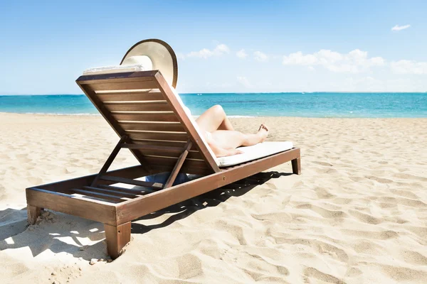 Mujer tomando el sol en la silla de cubierta en la playa — Foto de Stock