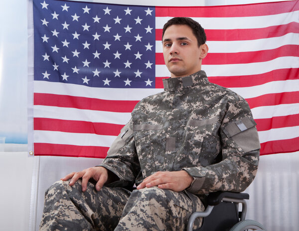 Патриотический солдат сидит на кресле-каталке против американского флага

