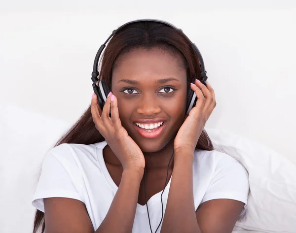 Mujer disfrutando de la música a través de auriculares en la cama —  Fotos de Stock