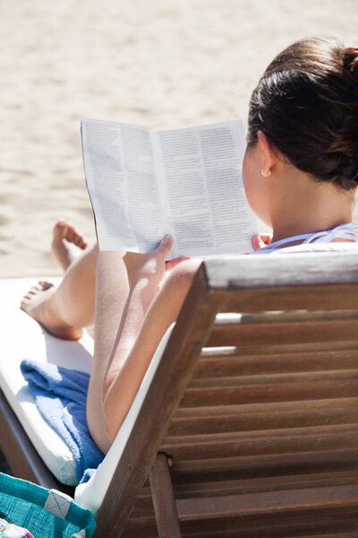 Woman reading book on deck chair at beach