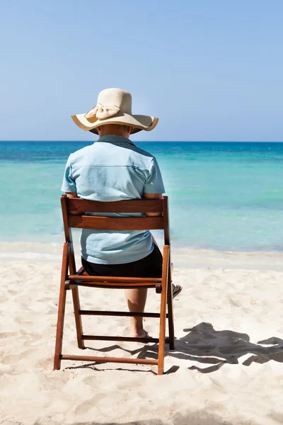 Kvinna sitter på stol vid stranden mot himlen — Stockfoto