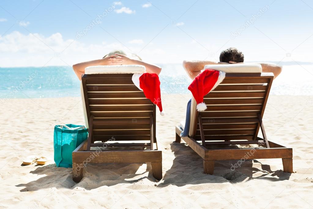 Couple with Santa hats relaxing on deck chairs at beach resort