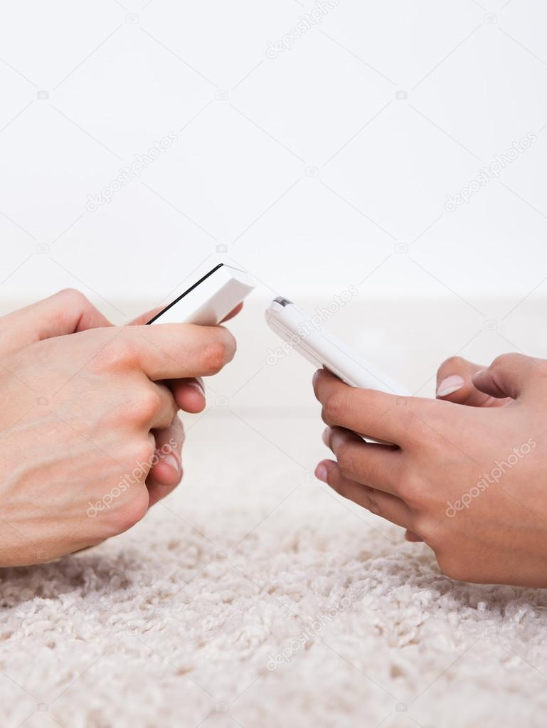 Hands Text Messaging Through Smartphones On Rug