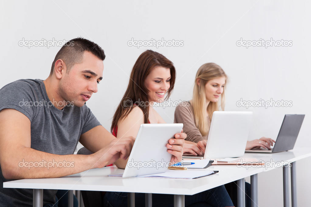 Confident Male Student Holding Digital Tablet At Desk