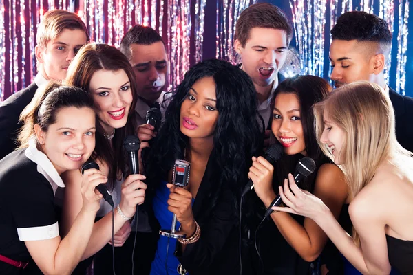 Amigos cantando en micrófonos en la fiesta de karaoke —  Fotos de Stock