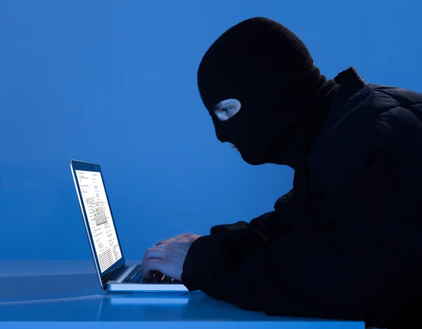 Criminal usando el ordenador portátil para hackear datos en la mesa — Foto de Stock