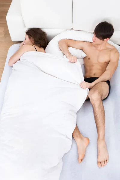 Homem puxando edredão de dormindo mulher no cama — Fotografia de Stock