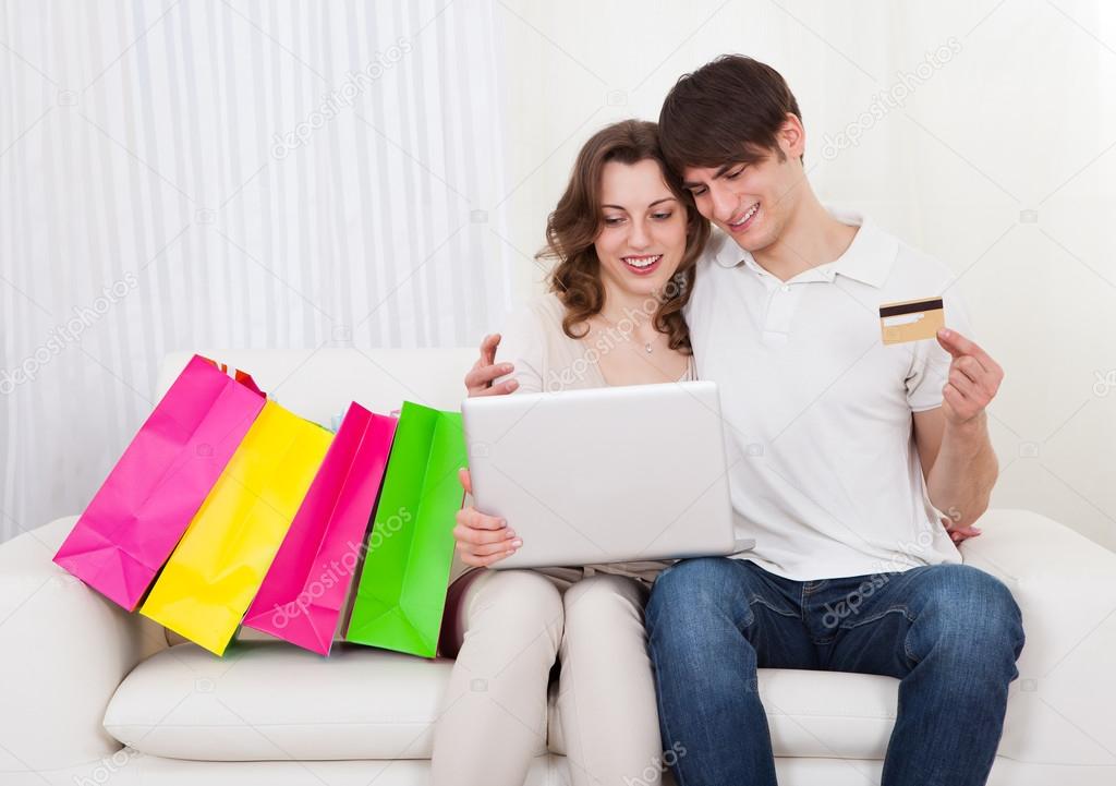 Happy couple sitting on couch shopping online