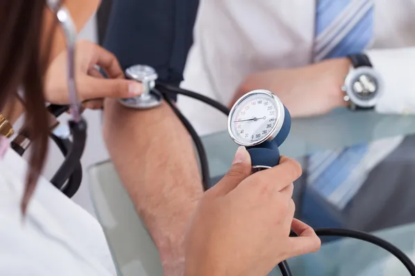 Médico revisando la presión arterial del hombre de negocios — Foto de Stock