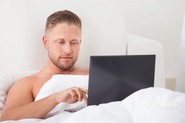 Hombre sentado en la cama trabajando en un portátil — Foto de Stock