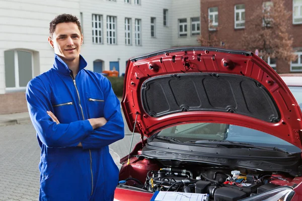 Vertrouwen mechanic met armen doorkruist staande door auto — Stockfoto