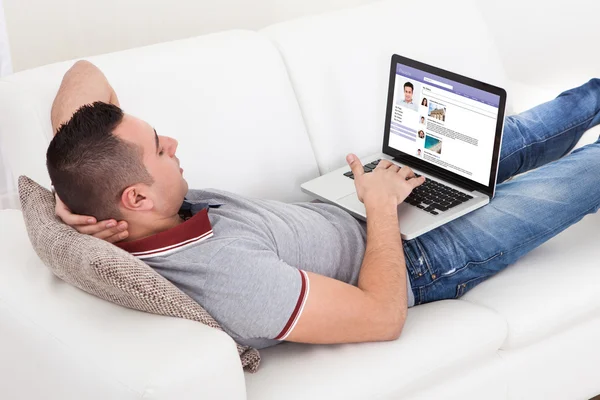 Man chatten op laptop terwijl liggend op de Bank — Stockfoto